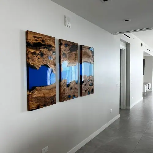 Three large wood and blue resin art panels hung on a long hallway wall