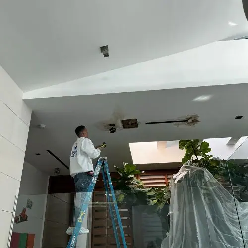 Worker on a blue ladder repairing stained spots on a high ceiling